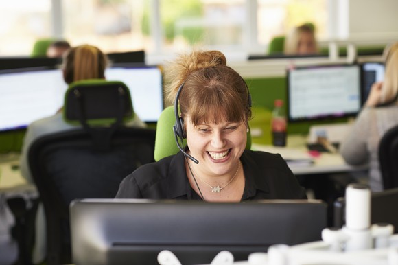 A smiling female customer service rep in front of her desktop in an office. 