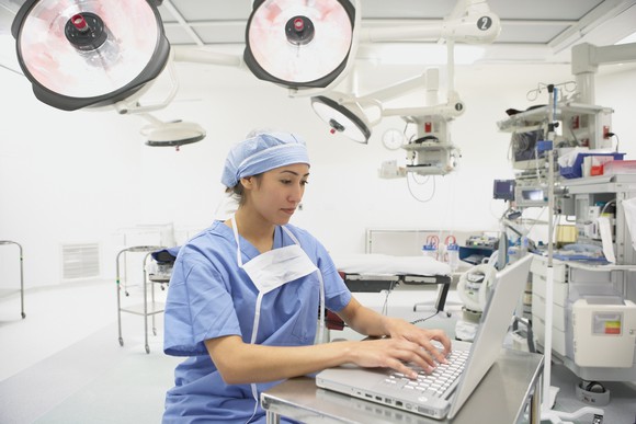 Physician typing on laptop in an operating room. 