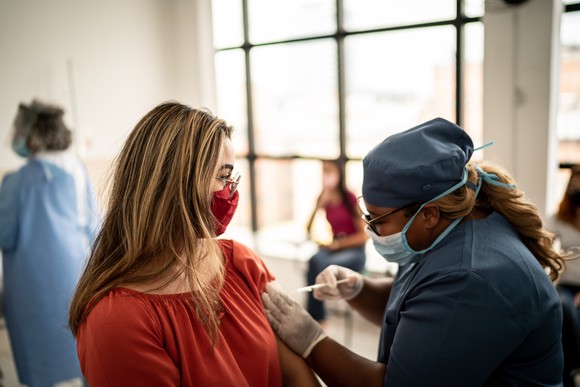 A healthcare worker gives an injection to a patient wearing a face mask.