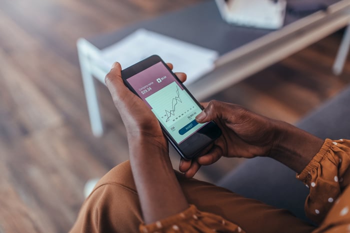 Person's hands holding a smartphone with a stock chart on display.