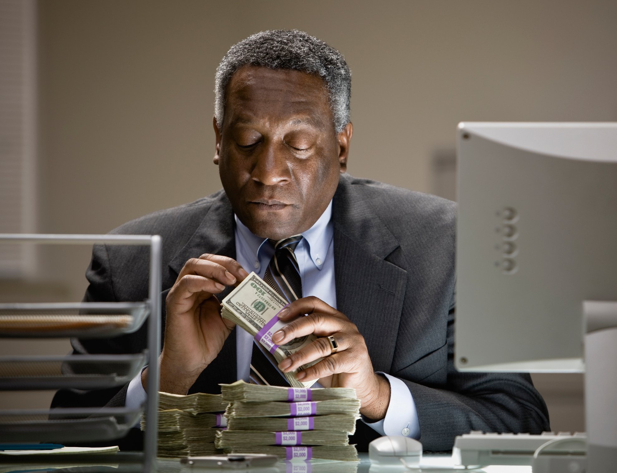 Worker investigates piles of $100 bills by a computer terminal.