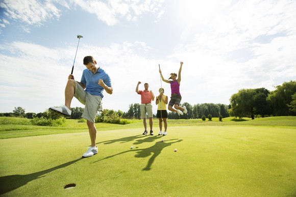 A group of four friends celebrating a success on a golf course under a sunny sky. 