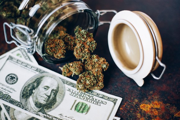 Marijuana bud spilling from jar onto $100 bills