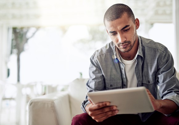 Man seated on couch is using tablet.