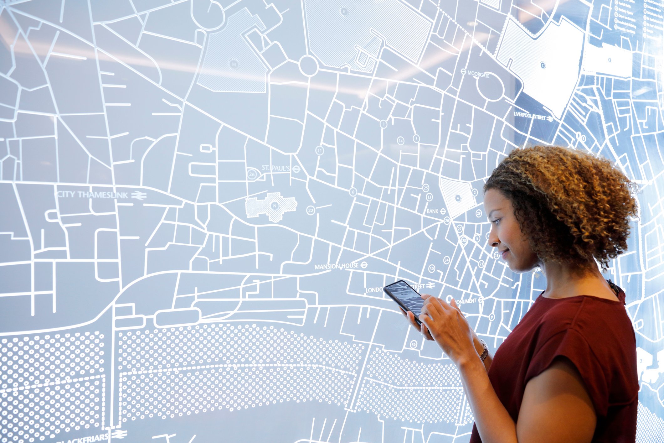 Woman on her phone in front of a map of a city on the wall.