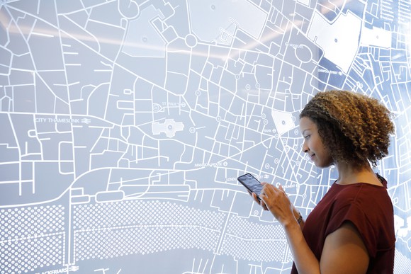 Woman on her phone in front of a map of a city on the wall.