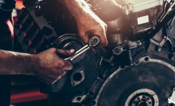 A person using a ratchet on a car engine.