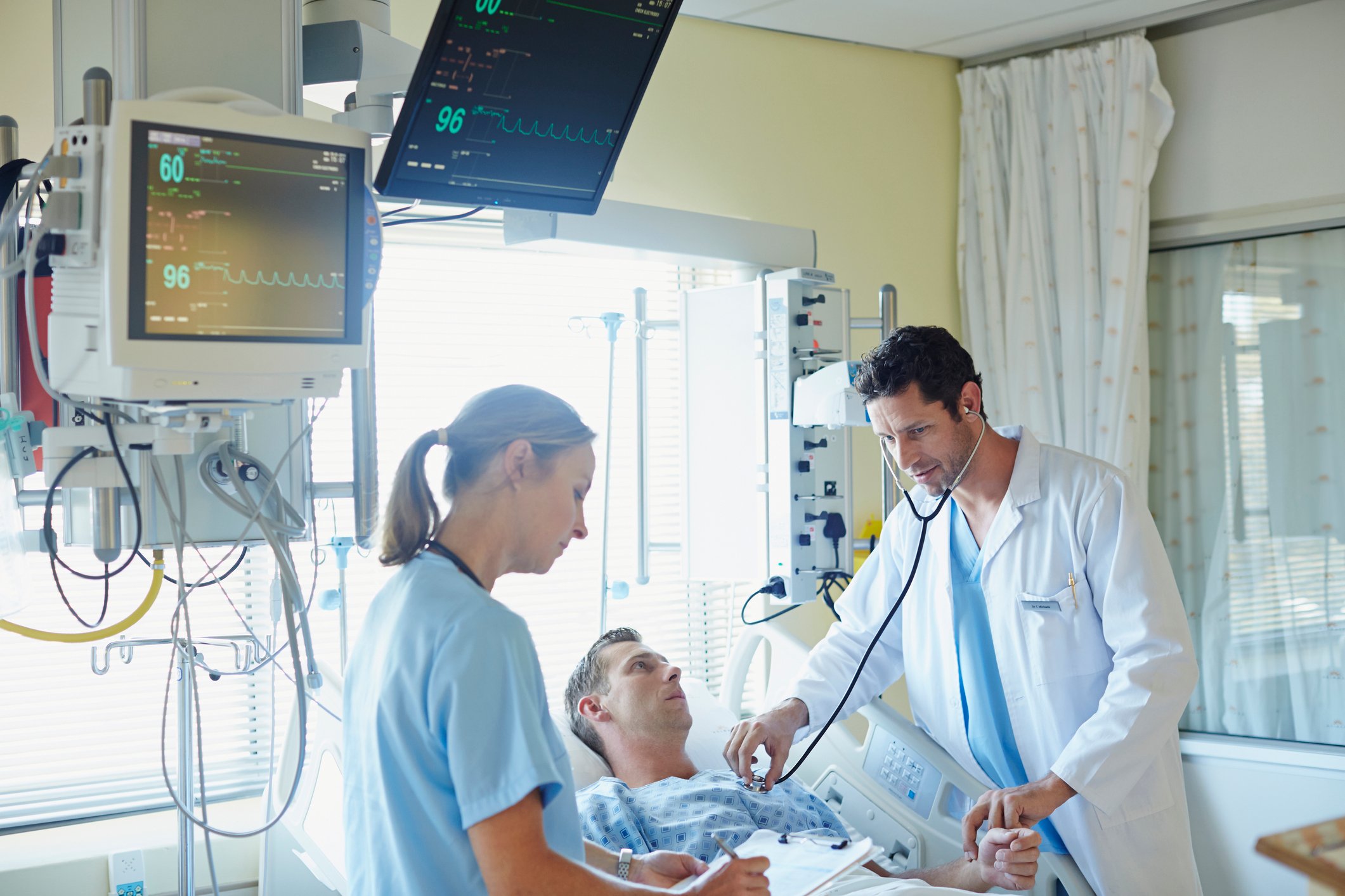 A doctor and nurse lean over a patient in a hospital bed.
