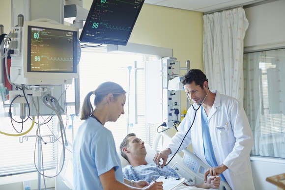 A doctor and nurse lean over a patient in a hospital bed.