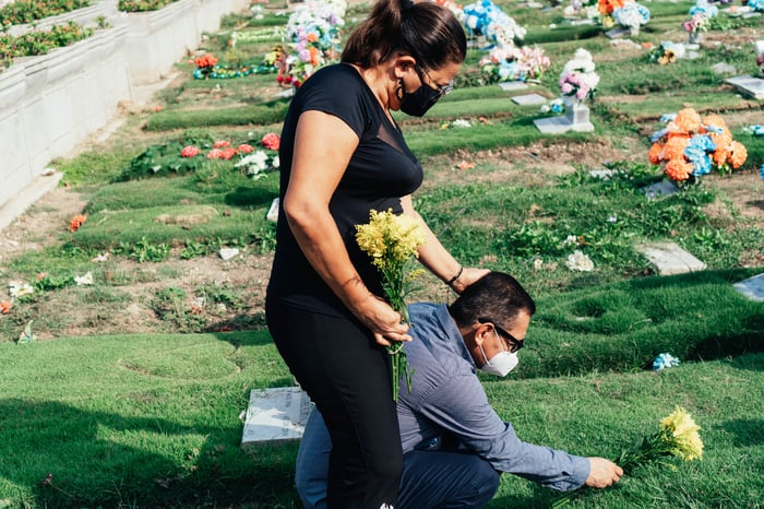 Two people with flowers at a grave site.