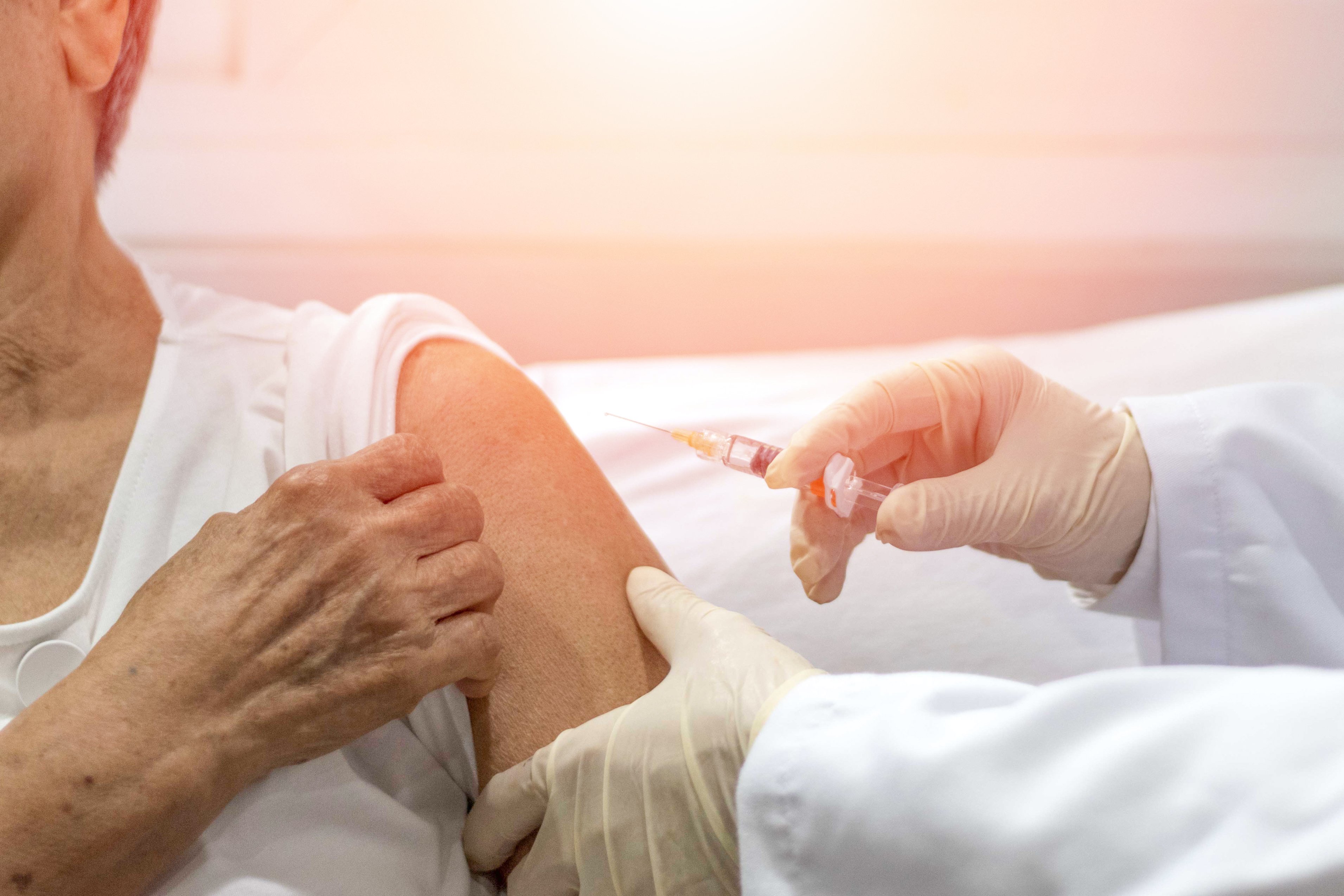 Gloved hands holding a syringe with needle near a person's arm.