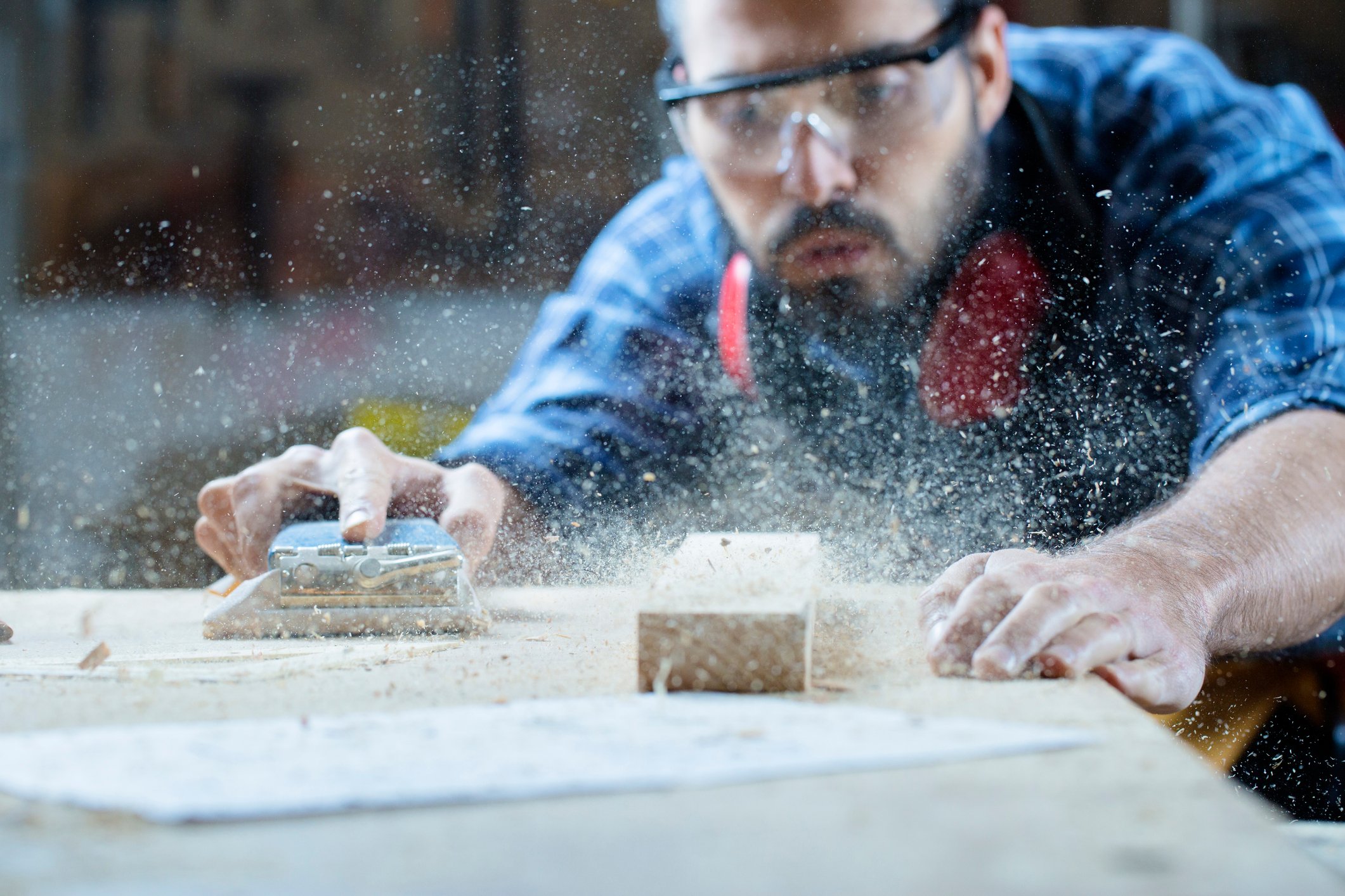 A carpenter is blowing sawdust off a wooden table. 