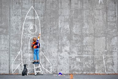 A boy draws a rocket on a wall.