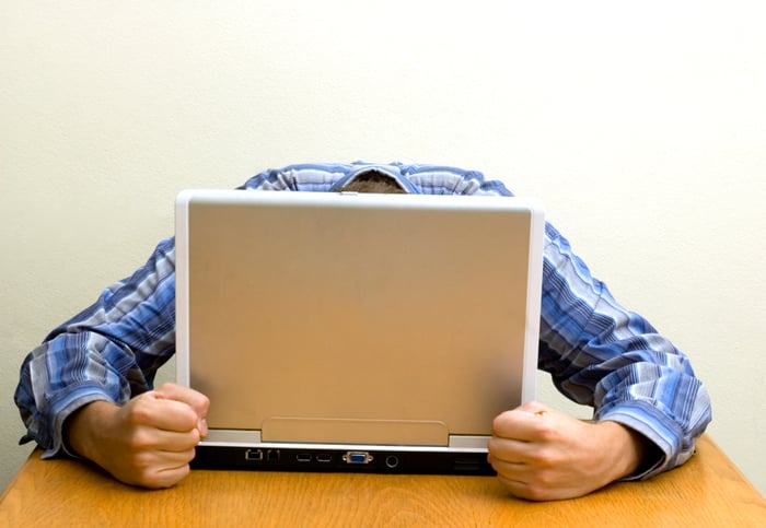 A person sitting at a desk with their head on a laptop computer.