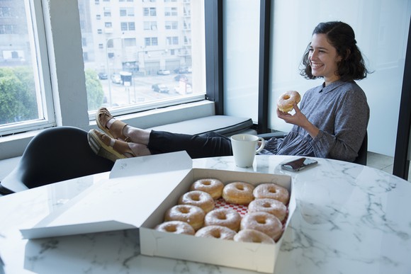 Person sitting in a chair with feet on window cell enjoying a box of donuts in a conference room.