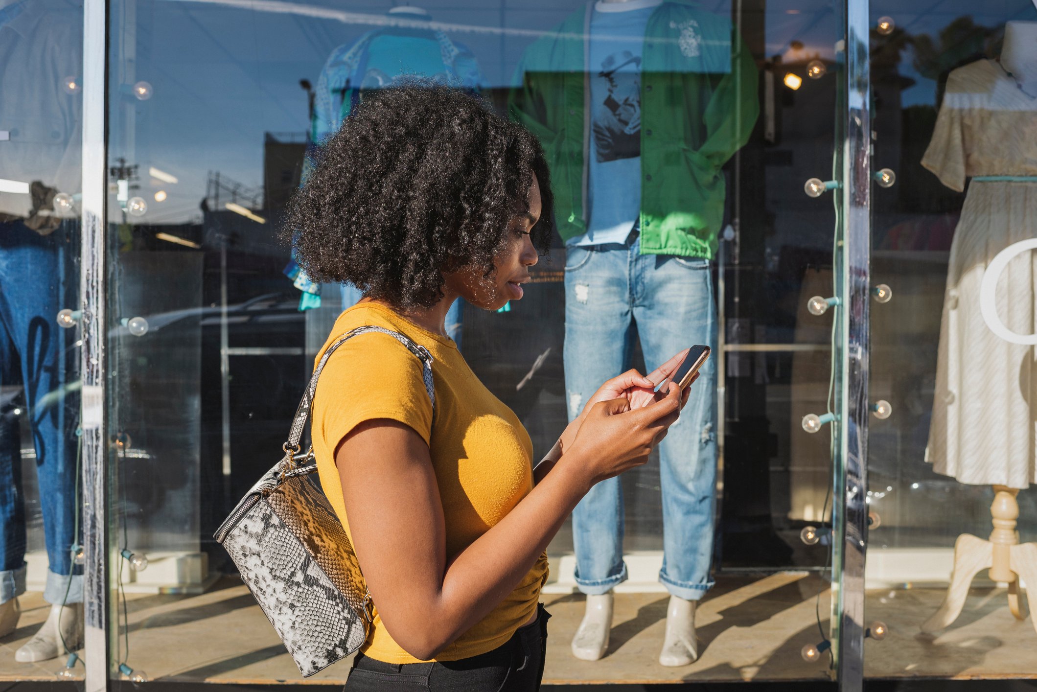 A young person standing outside a shop window looking at her phone.