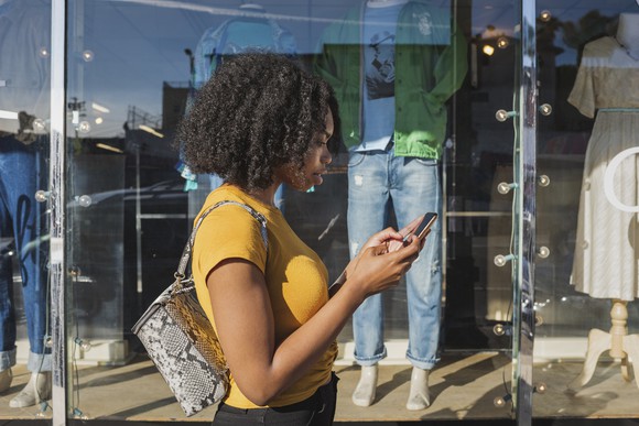 A young person standing outside a shop window looking at her phone.