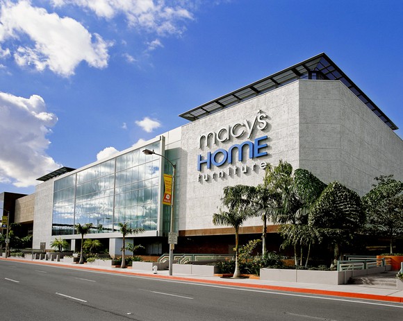 The sunlit front of the Macy's store in Costa Mesa, CA, under a blue sky.