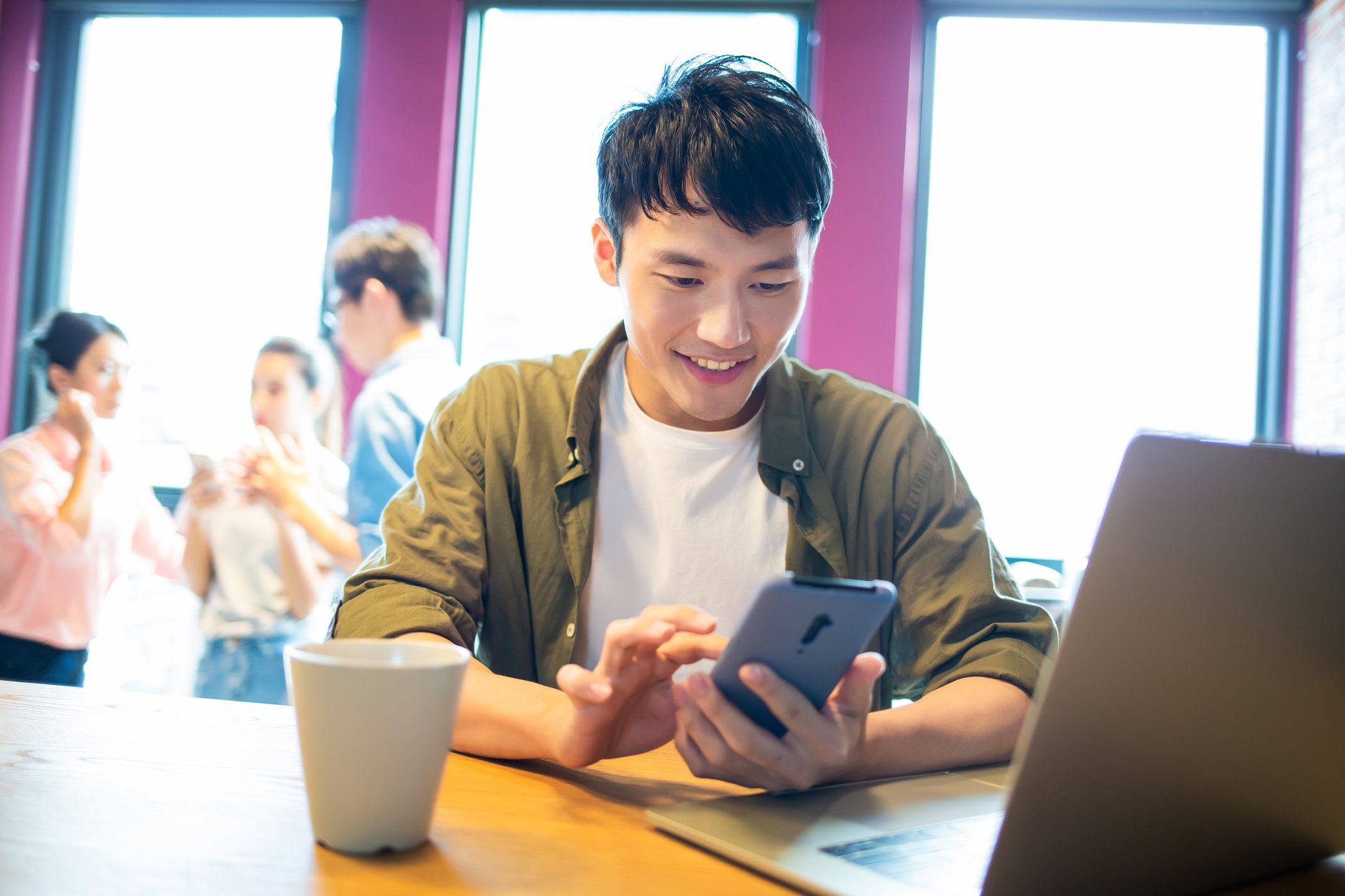 A smiling person uses a smartphone at a coffee shop.
