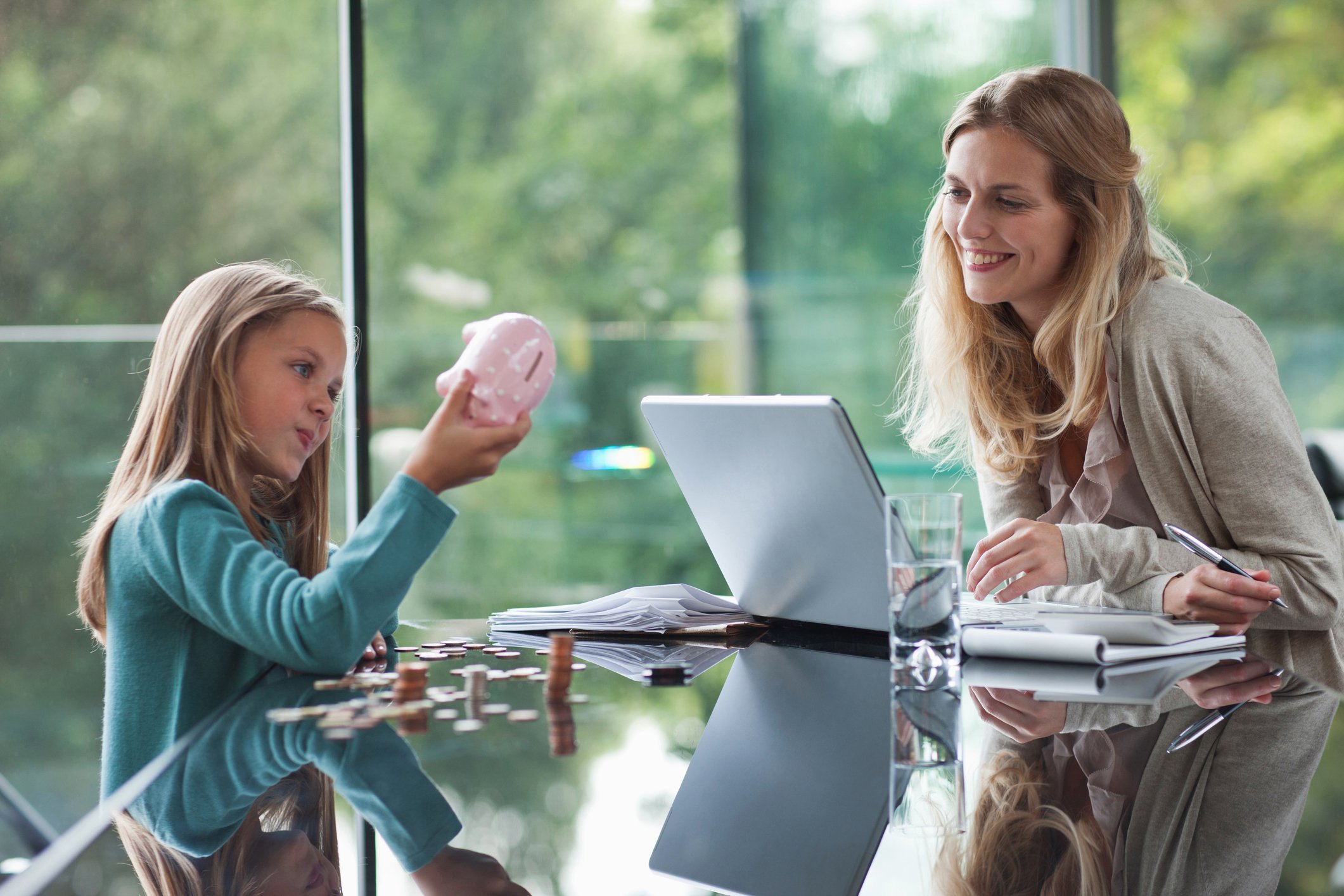 young child shaking coins out of piggy bank as smiling mother watches