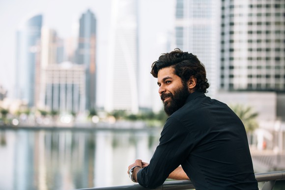 Bearded man wearing turtleneck looking out at city skyline.
