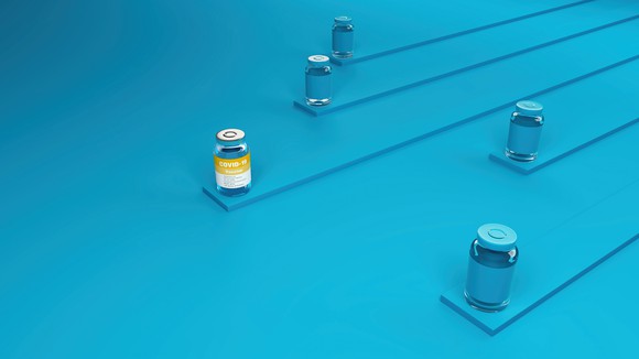 Four COVID-19 vaccine vials colored blue with one vial with an orange and white label in front of the others.