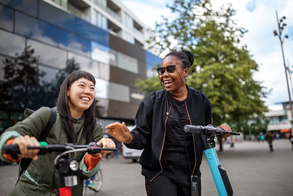 Two people riding scooters in a city.