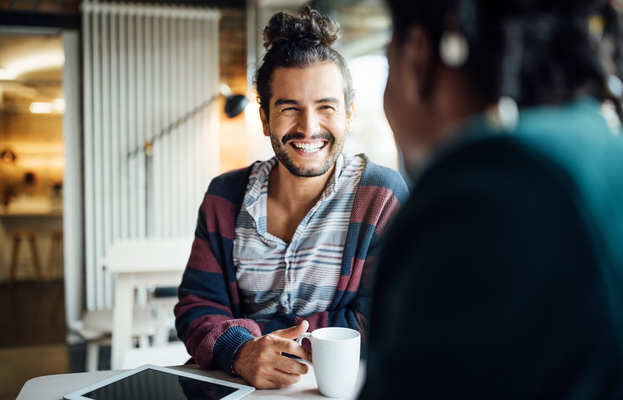 hipster man with bun sitting and drinking coffee with friend