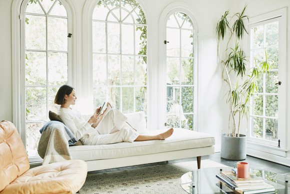 woman wearing white sitting in brightly lit sunroom reading