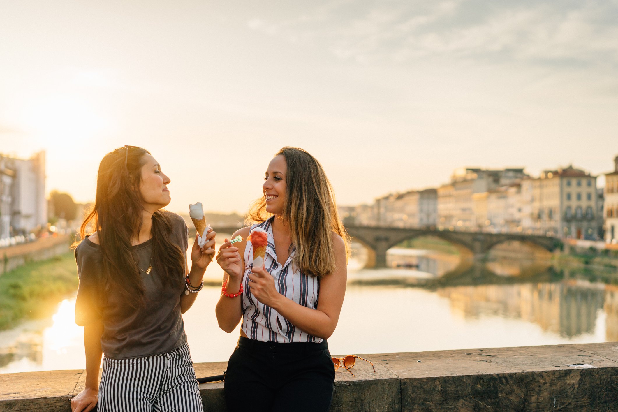two travelers eating gelato against the backdrop of the Arno River in Florence Italy