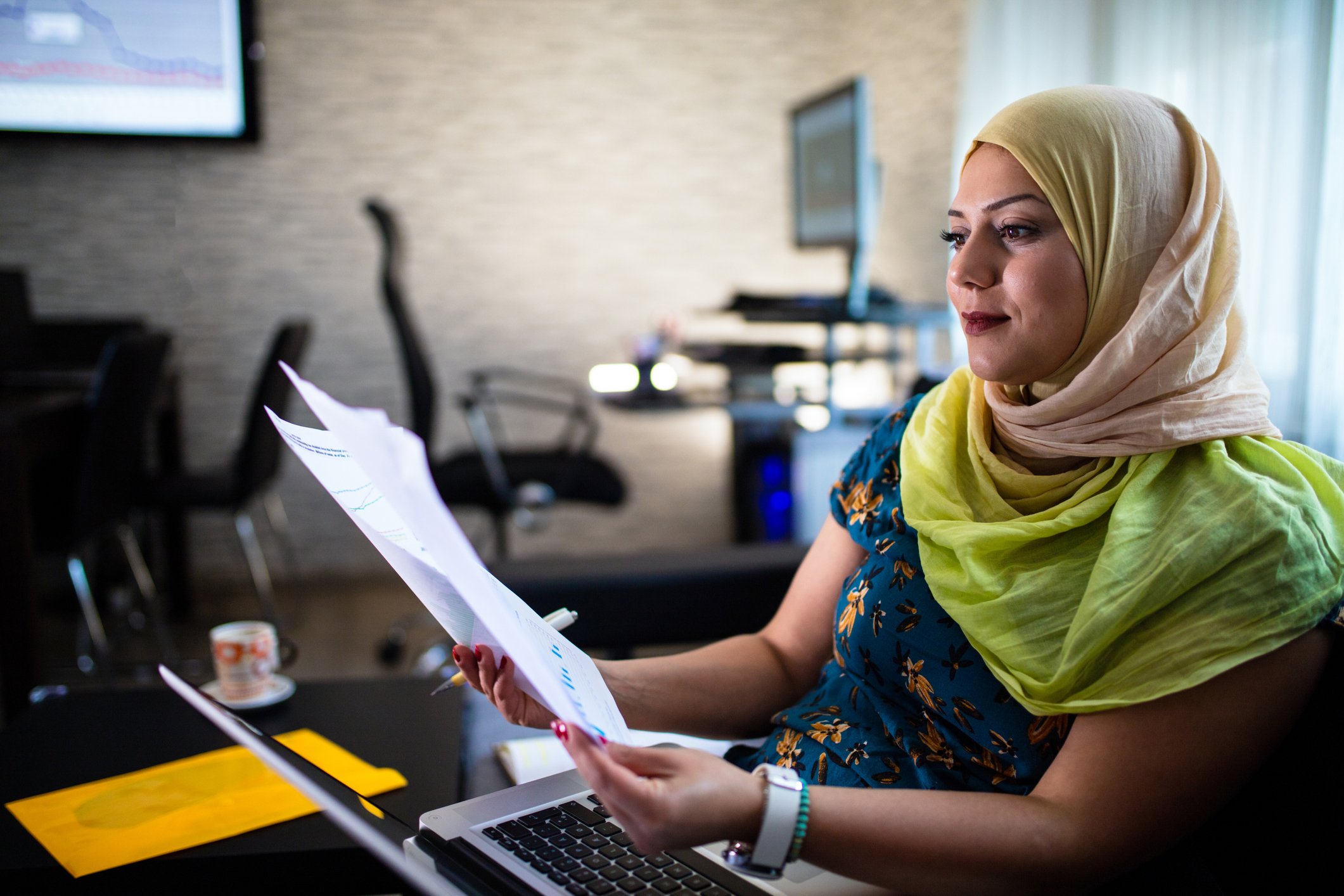 young person wearing brightly colored headscarf reviewing financial documents