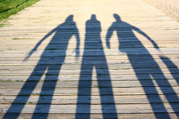 Shadows of three people on a boardwalk.