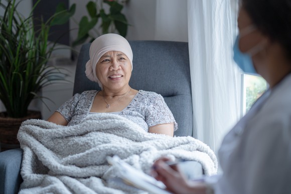 A cancer patient in a chair talking to a doctor.