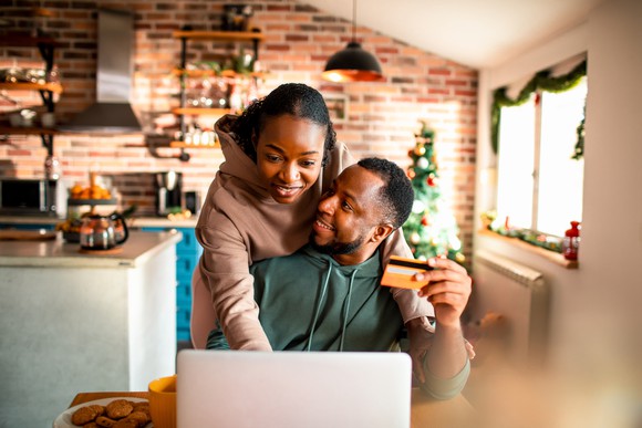 A couple uses a credit card while looking at a laptop at home.