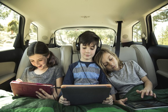 Three kids on tablets in the backseat of a car.