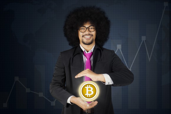 A smiling man holds up a giant Bitcoin token.