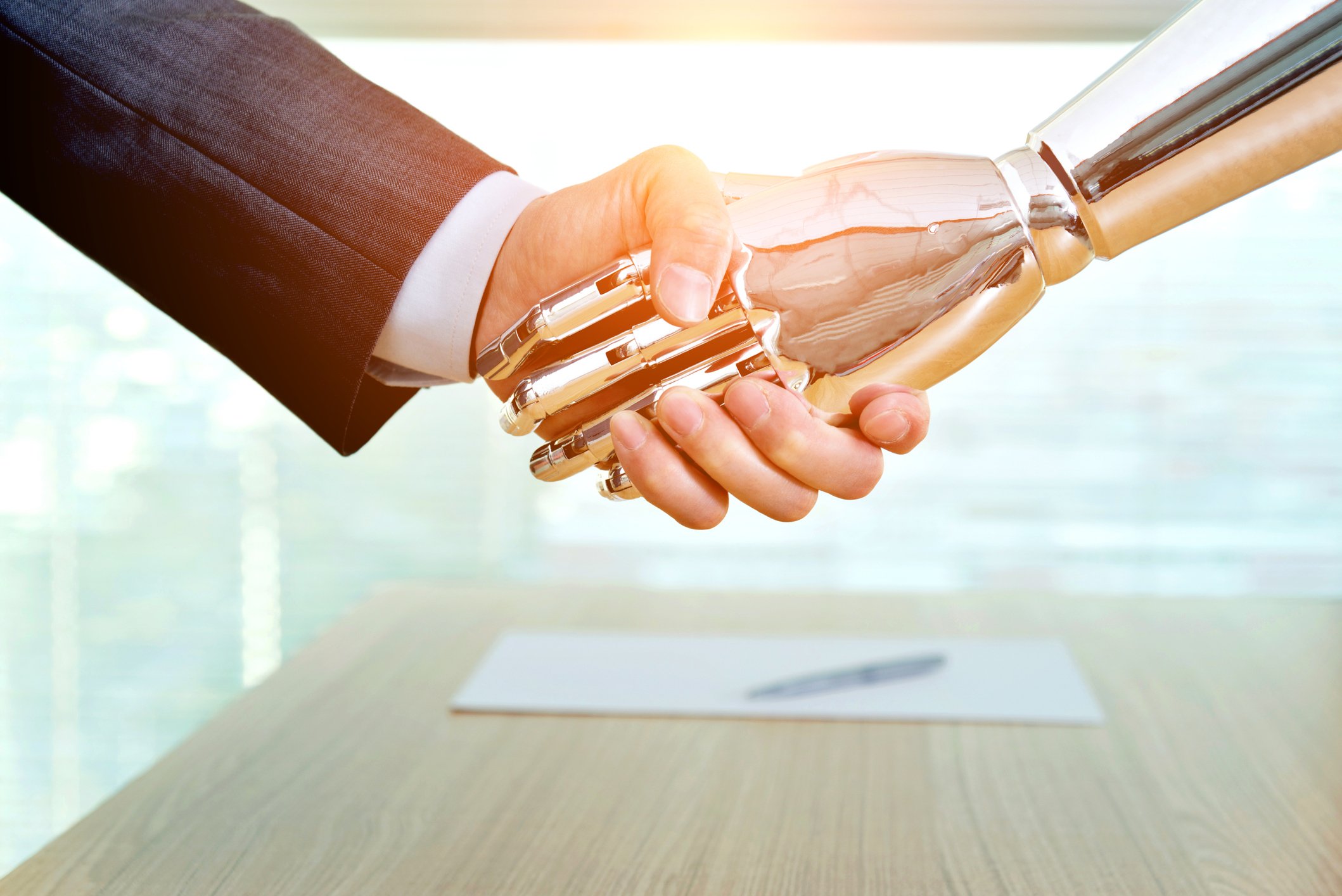 A businessman shaking hands with a robotic hand with a chrome and gold finish.