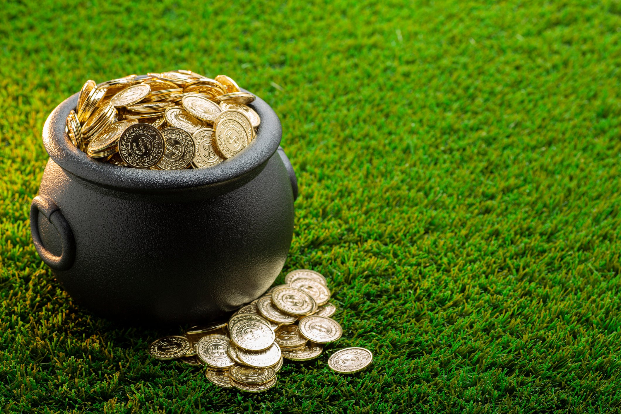 A cast-iron bucket full of gold coins on a green lawn.