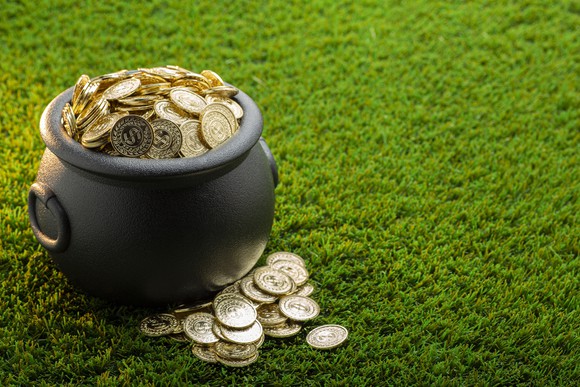 A cast-iron bucket full of gold coins on a green lawn.