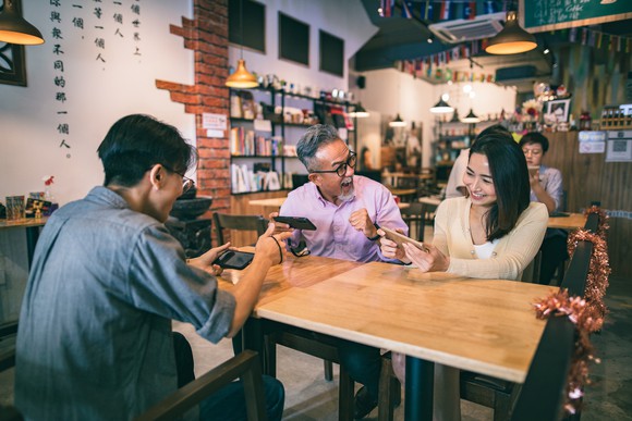 Three people playing mobile games in a restaurant.