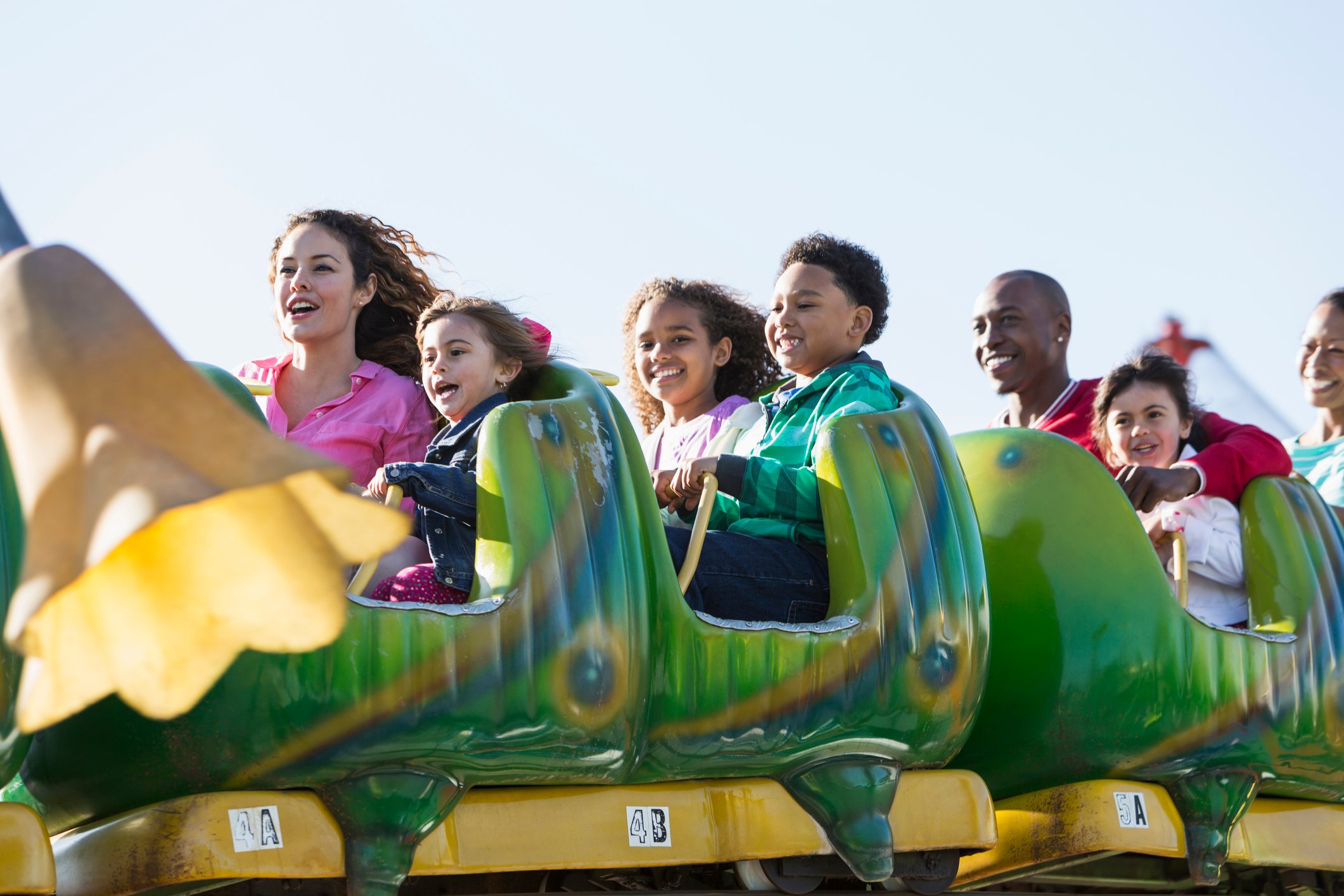 Seven smiling people on a green amusement park ride.