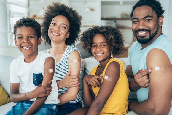 A family all showing off the Band-Aid on their arm from getting a shot.
