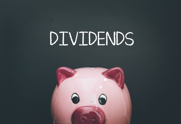 A piggy bank in front of a chalkboard with "Dividends" written on it.