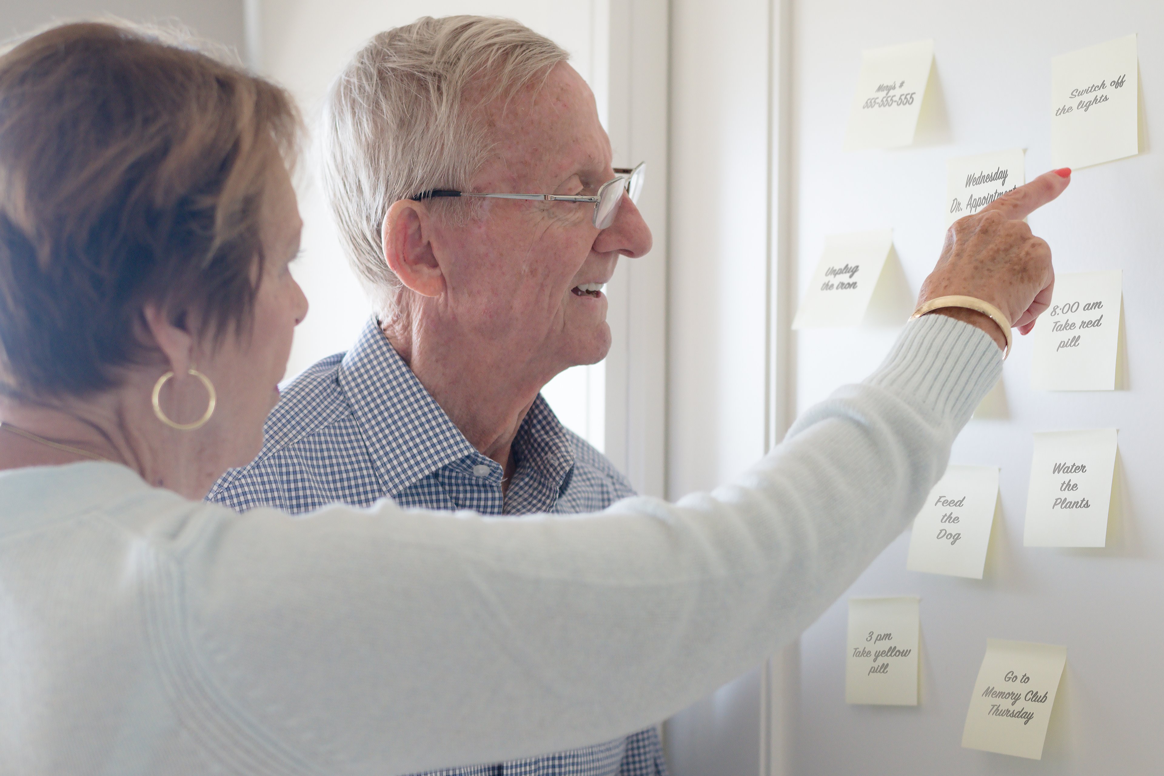 Elderly couple pointing and looking at sticky notes reminders.