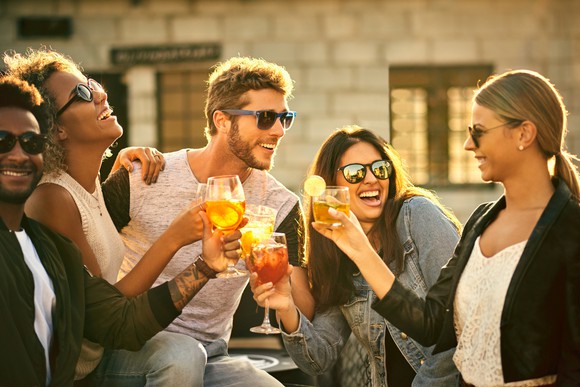 Group of five friends having drinks and smiling outside.