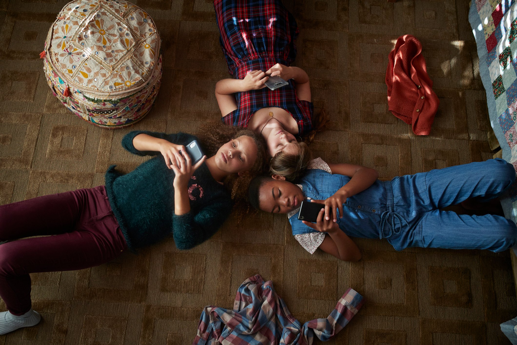 Three kids laying on the floor using their smartphones.