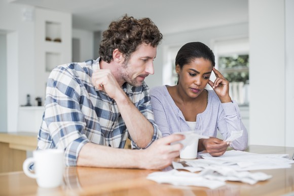 A couple looks troubled as they consider printouts over coffee at their dining-room table.