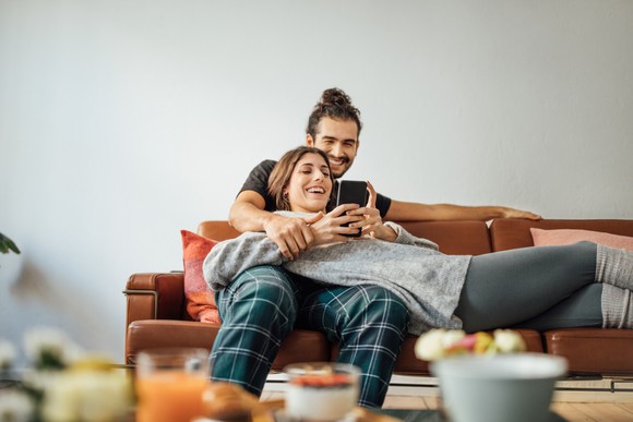 Two smiling people on a couch looking at a cell phone.