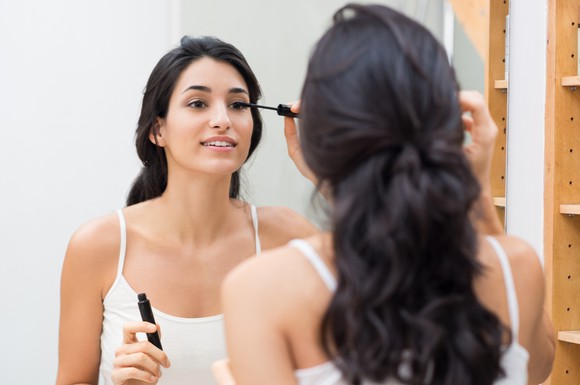 A woman putting on eye makeup in the mirror