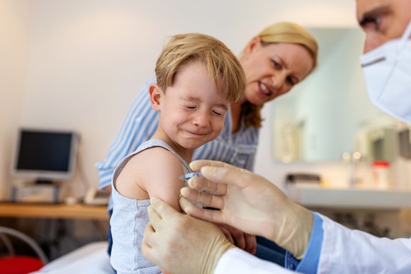 A small child reacts in pain to an injection in their right arm.